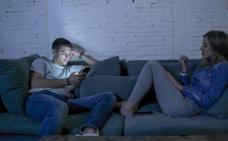 A man and a woman are sitting on a couch looking at their phones.
